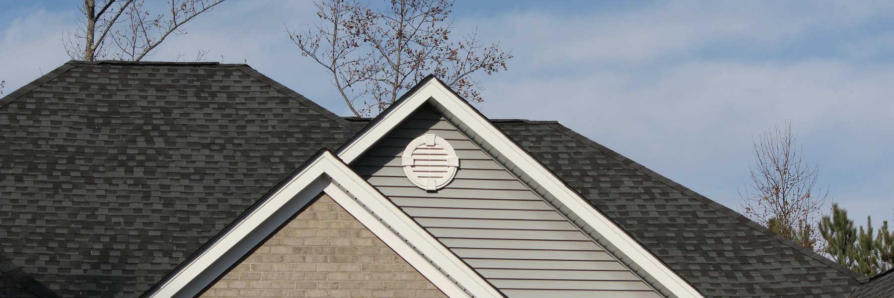 Asphalt shingle roof and gray siding gable under a cloudy sky