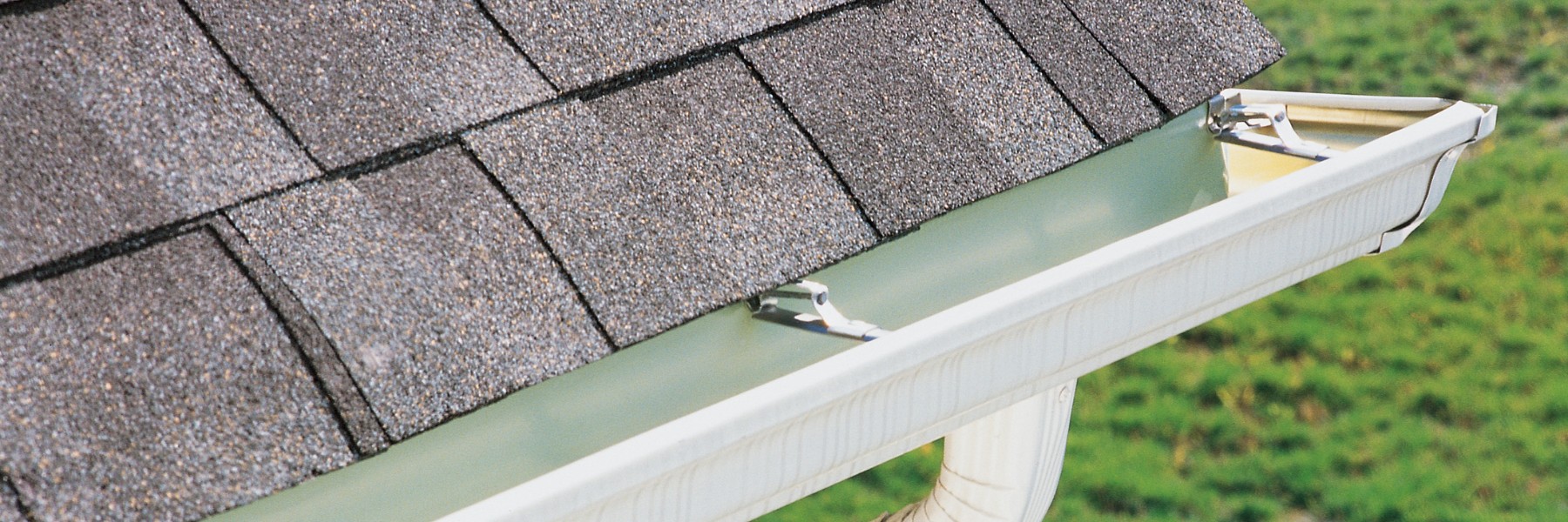 White gutter and downspout below an asphalt shingle roof